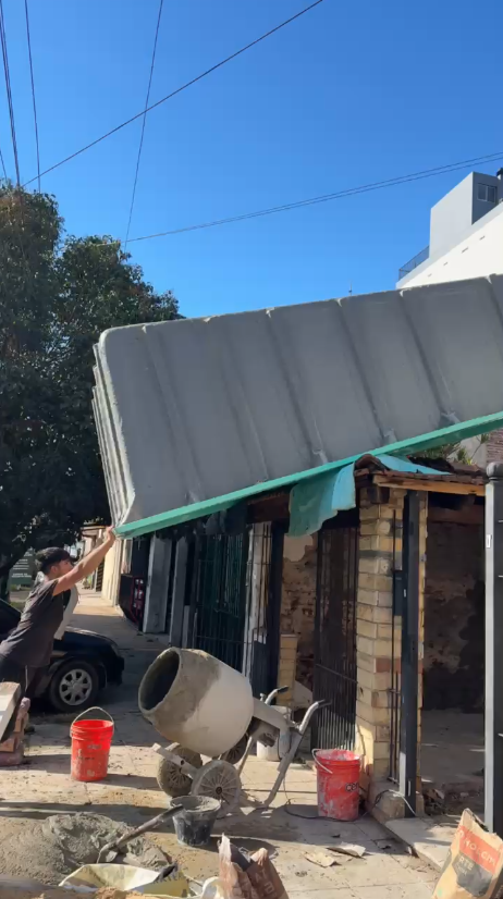Operario sosteniendo el borde de un casco de pileta de fibra de 7x3 elevado sobre el techo de una casa, visto desde la vereda