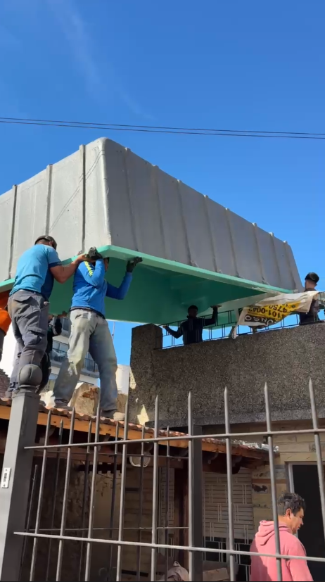 Equipo de seis operarios de Rodano pasando un casco de pileta de fibra por encima de la medianera de una casa